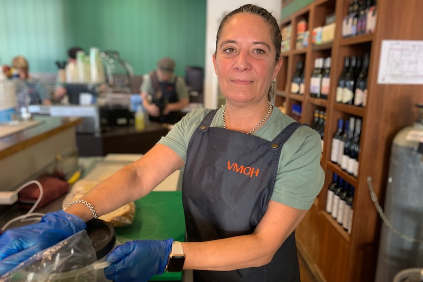 Cafe Coordinator Jodie Long stands behind a shop counter with blue gloves on.