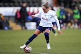 A woman soccer player wearing white and dark blue controls the ball on the grass