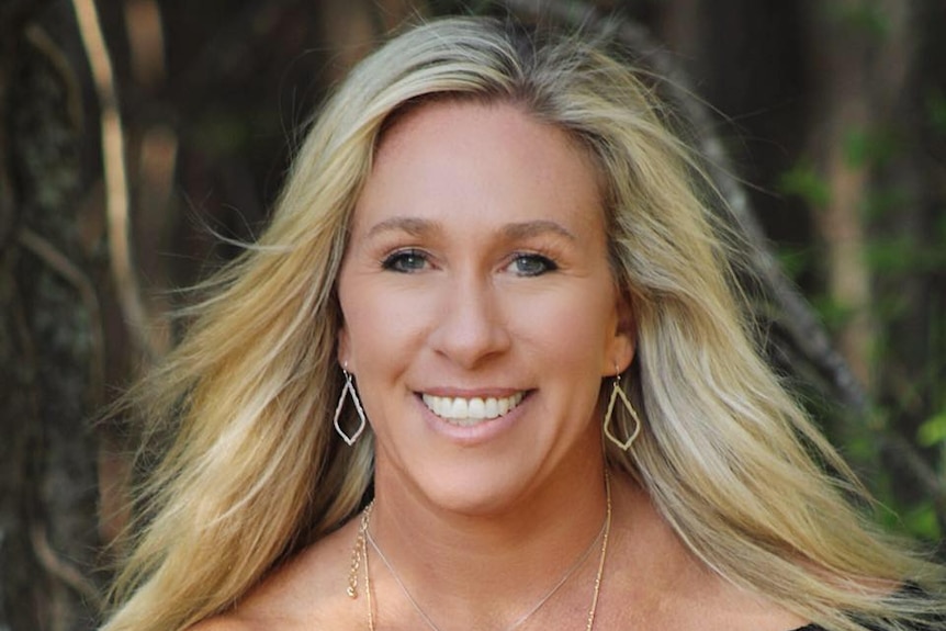 A 40-plus woman with long blonde hair in black designer dress smiles at camera in outdoor setting.