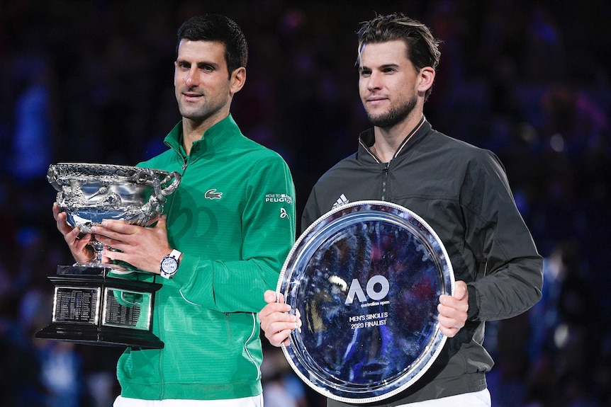 The two finalists in the Australian Open stand next to each other, one holding the winner's trophy.