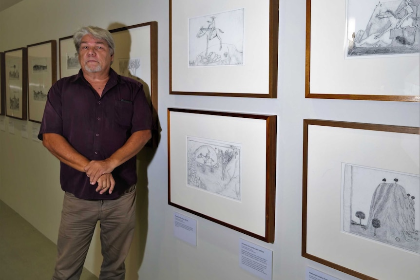 Man Standing beside framed drawings.