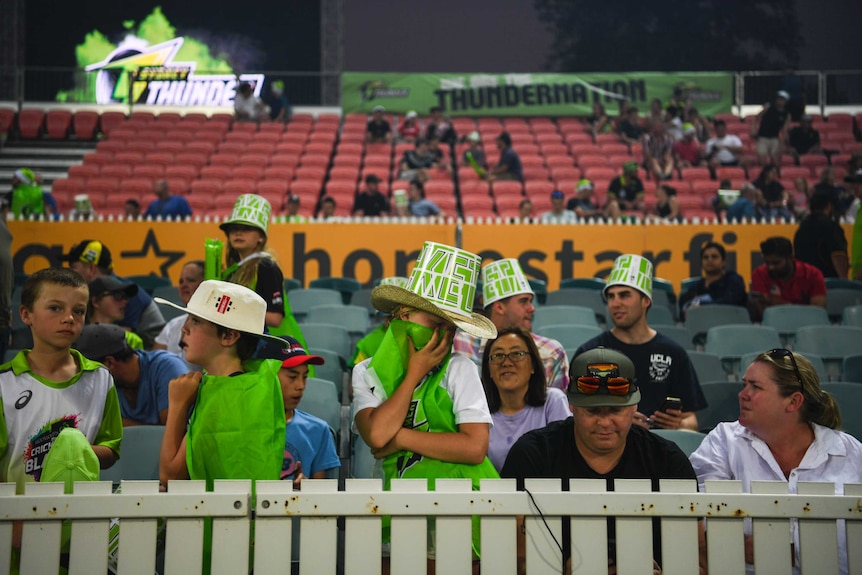 Children cover their faces with flags at a Big Bash match as smoke haze drifts into Manuka Oval