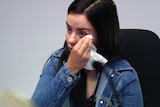 A young woman wipes away a tear while speaking at an inquiry into maternity services.