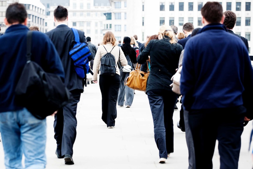 The backs of a group of adults walking, with the back of a woman wearing backpack and cream jacket at centre.