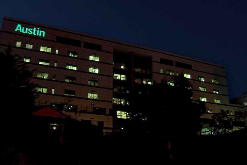 Large hospital building at night with word Austin illuminated above row of windows with lights on, under dark night sky