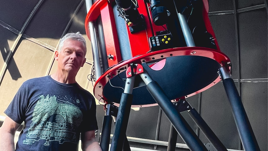 a man stands next to a large red telescope inside an observatory he has built in his garden