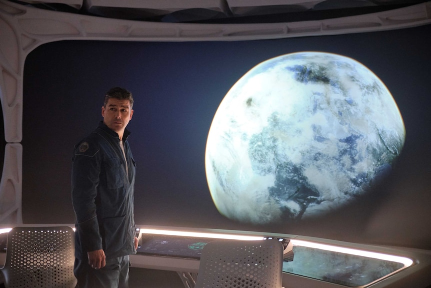 Actor Kyle Chandler stands in a space ship, the earth just outside the window, in the sci-fi movie The Midnight Sky