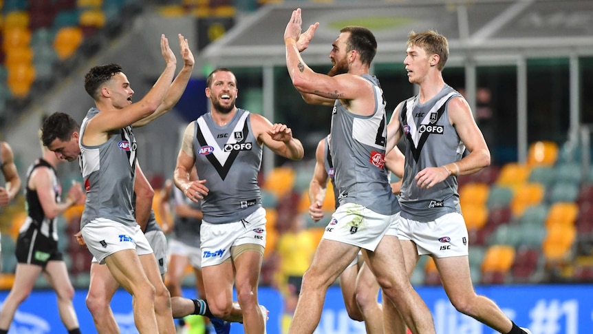 A tall forward puts his hands up to high five teammates after kicking a goal in an AFL game.