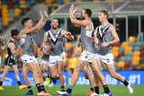 A tall forward puts his hands up to high five teammates after kicking a goal in an AFL game.