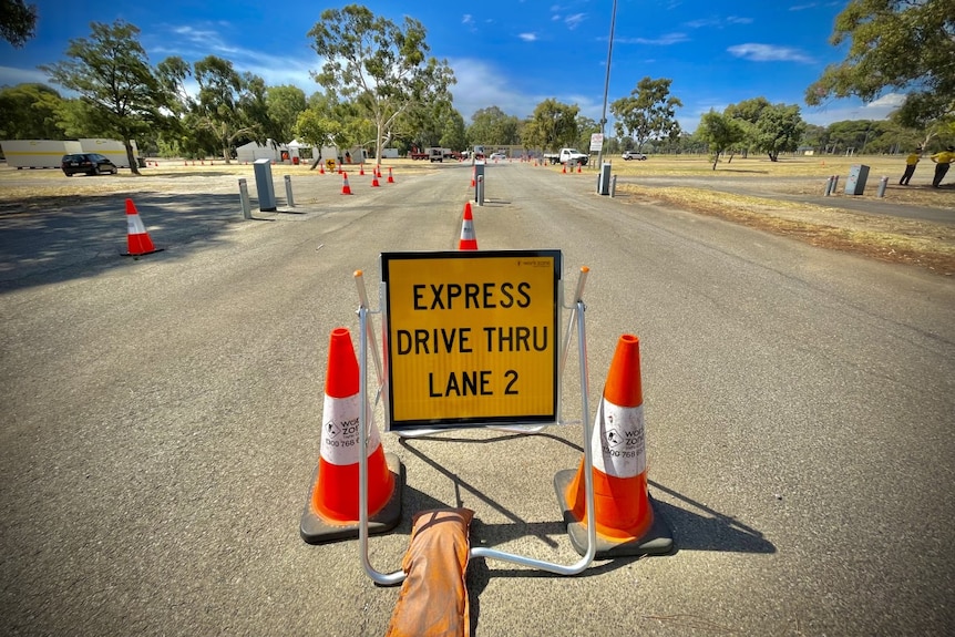 A yellow road traffic a-frame sign reading 'express drive thru lane 2', with a line of orange traffic cones behind it