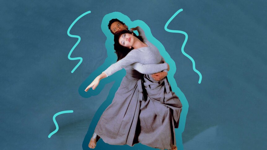 Kate Bush dances with a man who has his arms around her waist, against a teal background. They are both wearing all grey.