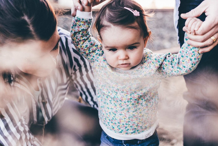 Parents holding the hand of a baby girl to depict work rights information after returning from maternity leave.