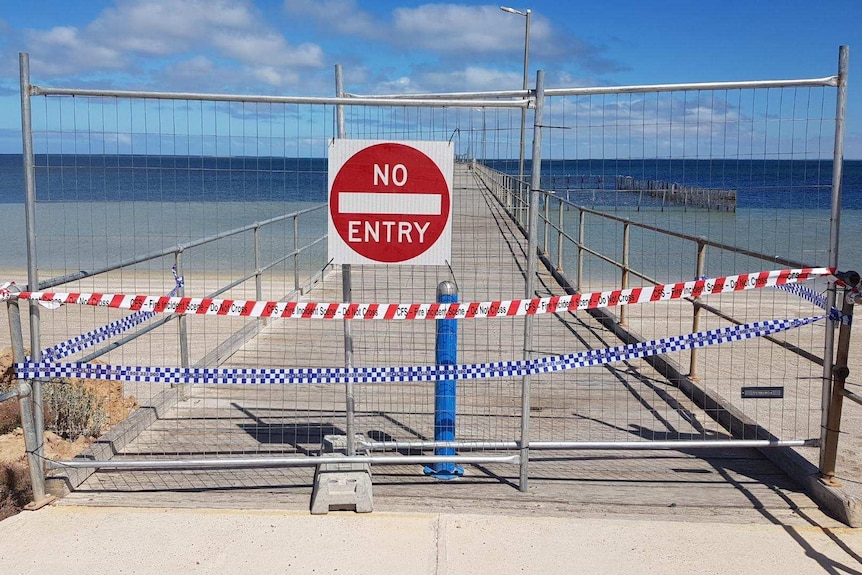 a no entry sign blocks access to a long jetty with a swimming pool enclosure on the right