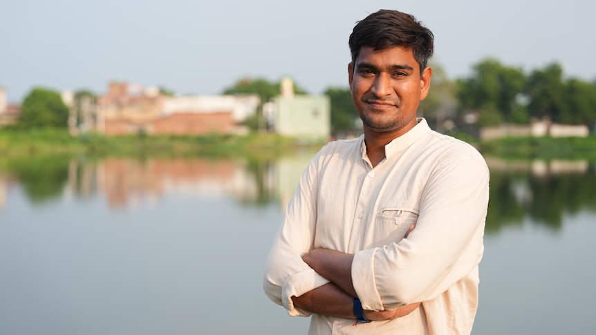 Ramveer Tanwar, wearing a white shirt, smiles as he stands in front of a pond.