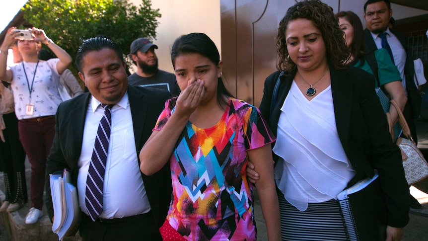 A young woman wipes her nose as she walks from court flanked by lawyers.