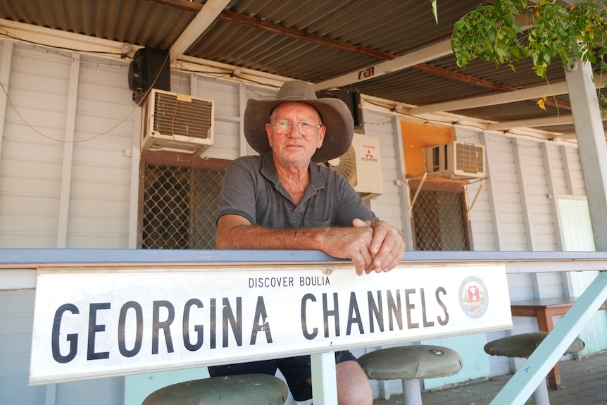 Older man wearing cowboy hat sits on a verandah