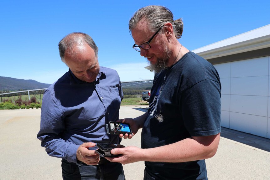 Two men look at an electronic device.