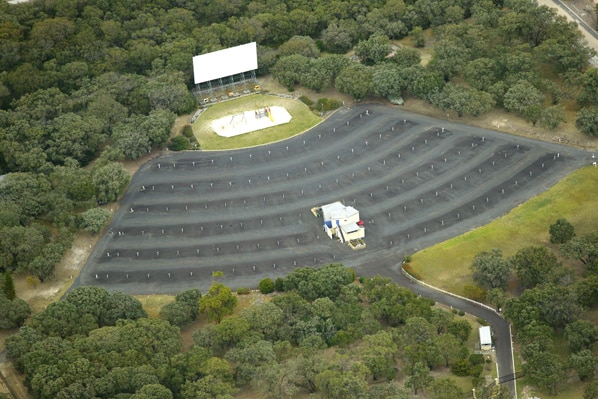 An aerial view of a drive-in cinema showing car spaces and a big screen.