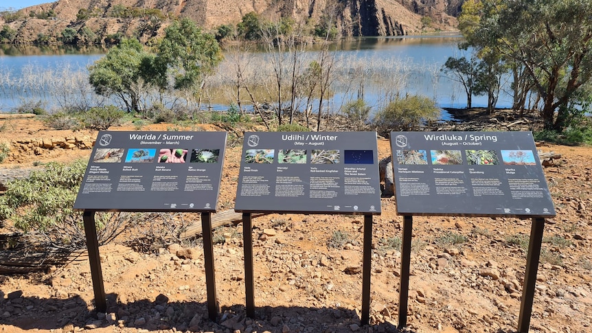 Three rectangle signs on an angle, with water and a mountain range in the background.