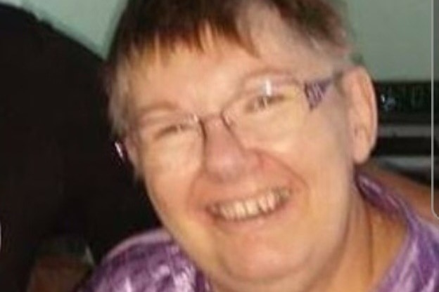 An older woman smiles while holding a watch.