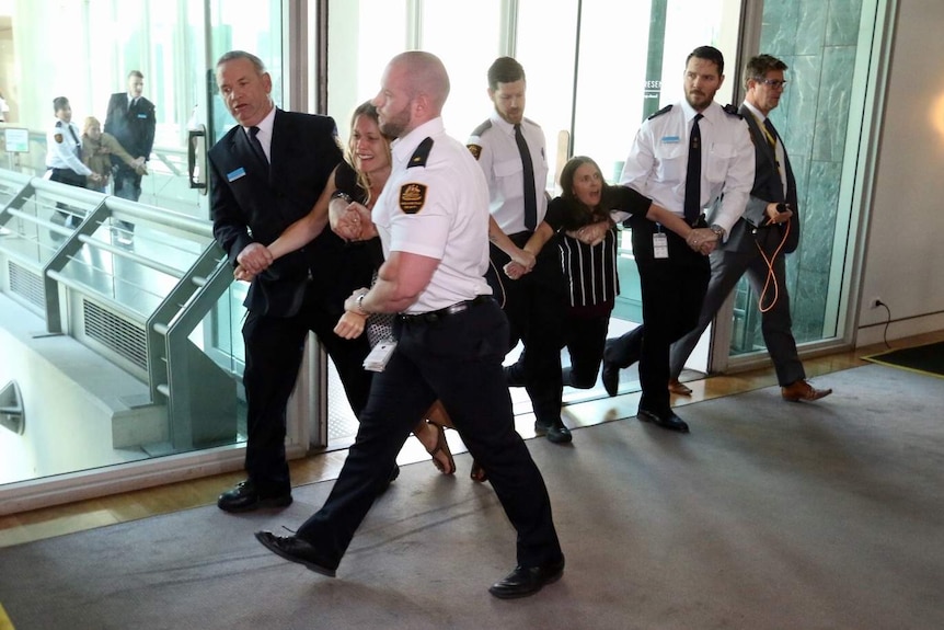 Two crying protesters being escorted out of Question Time by Parliament House security.