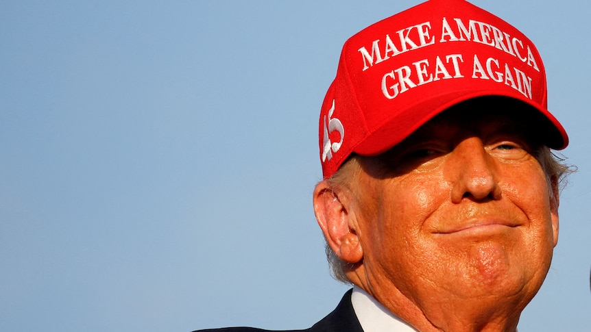 Donald Trump in a red cap smiles 