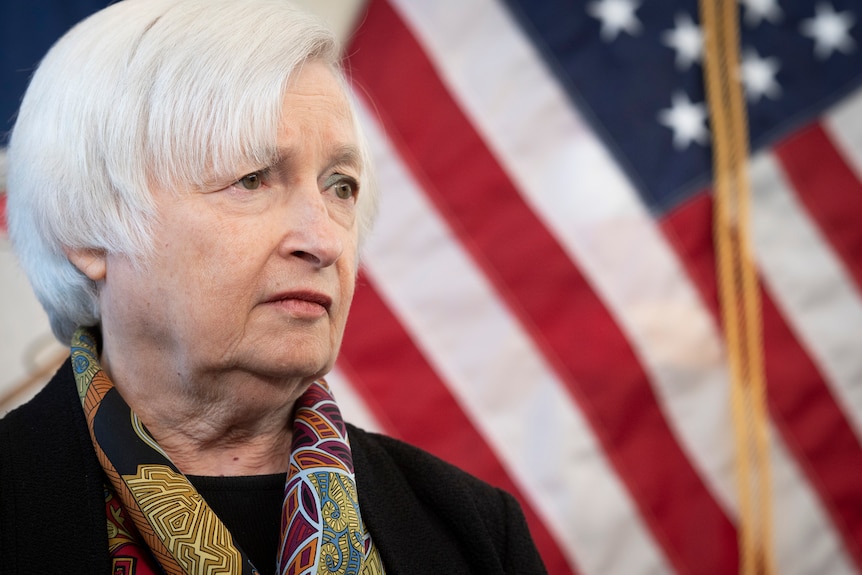 Treasury Secretary Janet Yellen speaks with reporters while standing in front of a US flag.