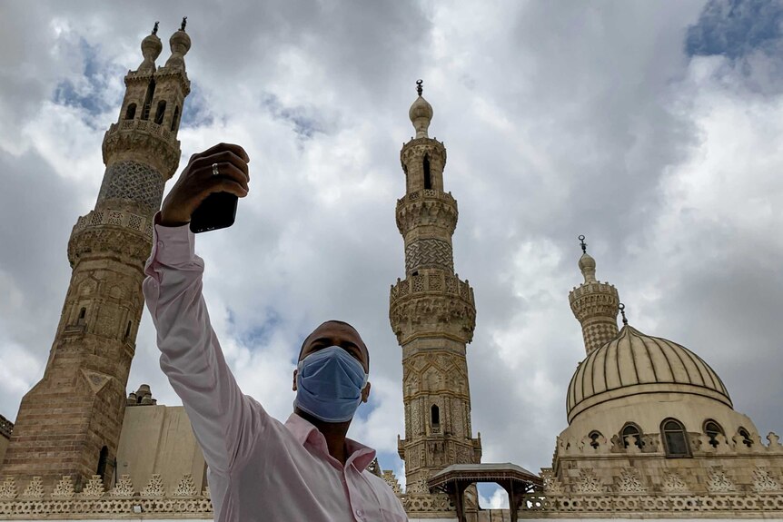 A man takes a selfie in front of the Al-Azhar mosque while wear a medical mask.