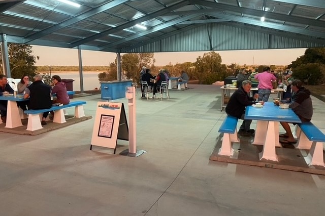 Travelers sit at tables eating in a caravan park. 