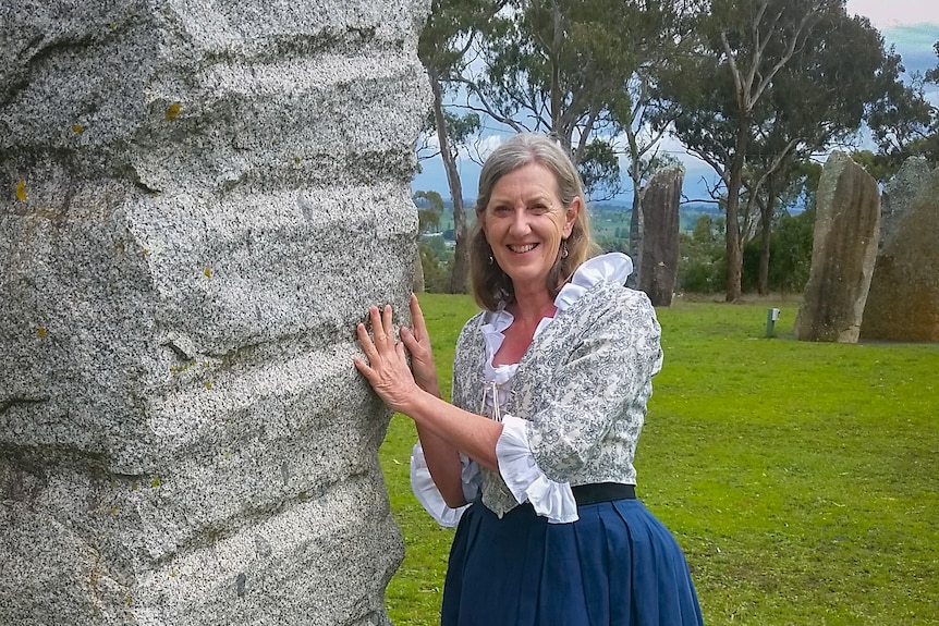 A woman dressed in period costume touches a granite standing stone