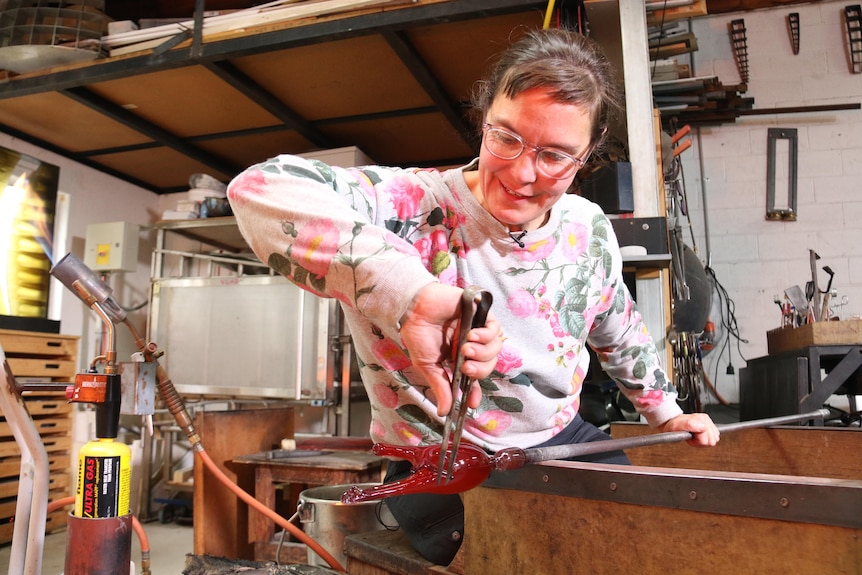 A woman leans over a kiln with glass, making a shape.