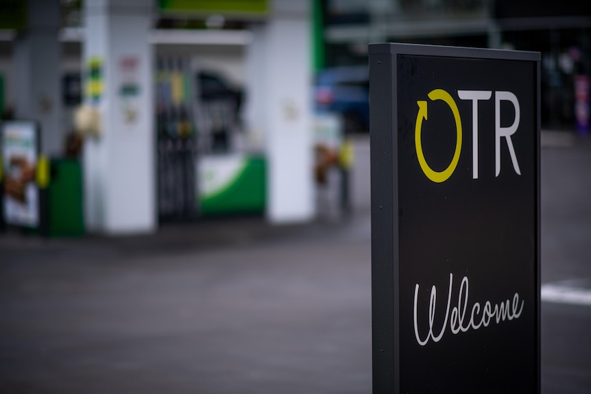 Black sign with the words OTR and welcome in front of a service station.