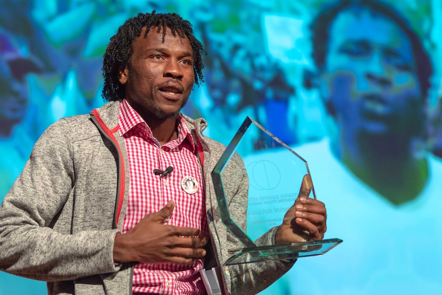 Abdul Aziz Muhama hold the Martin Ennals Award trophy as he speaks to the crowd.