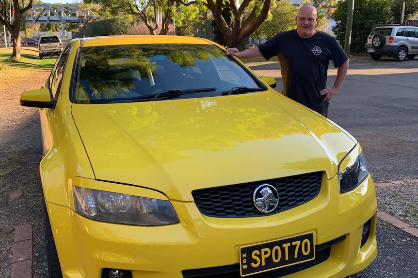 man standing with a yellow car with spotto number plate