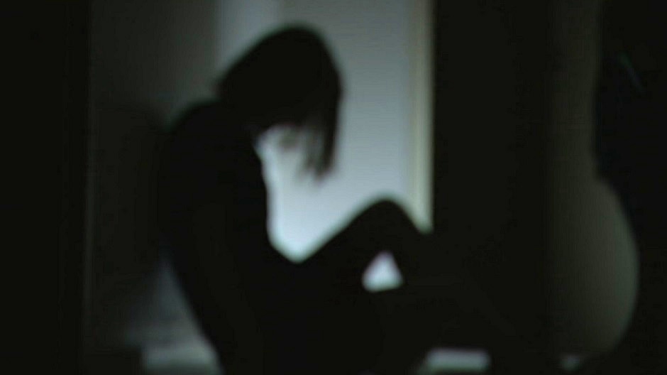 A blurry image of a woman sitting on the floor in shadow
