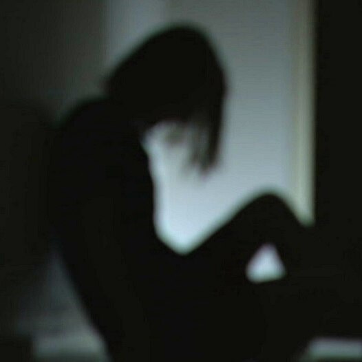 A blurry image of a woman sitting on the floor in shadow