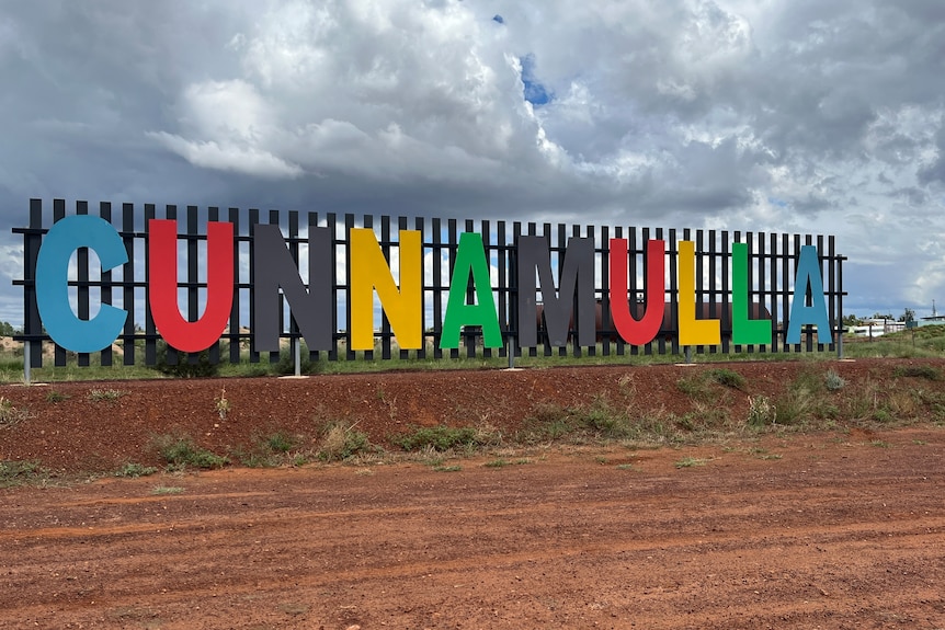 A big sign saying "Cunnamulla" in the outback. Each letter is a different bright colours.