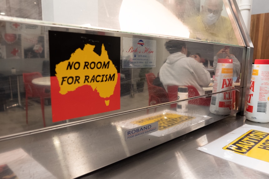 An anti-racism stikcer on a bain marie. A group of young people can be seen in the reflection of the stainless steel 