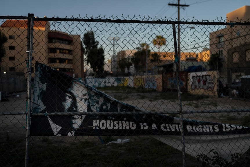 A banner falling off a chain link fence shows Martin Luther King Jr's face and says 'housing is a civil rights issue'. 