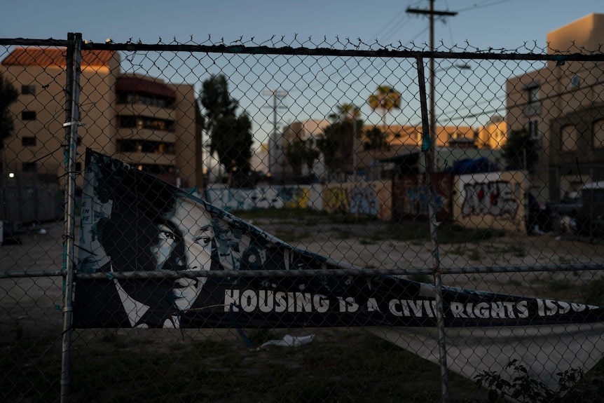 A banner falling off a chain link fence shows Martin Luther King Jr's face and says 'housing is a civil rights issue'. 