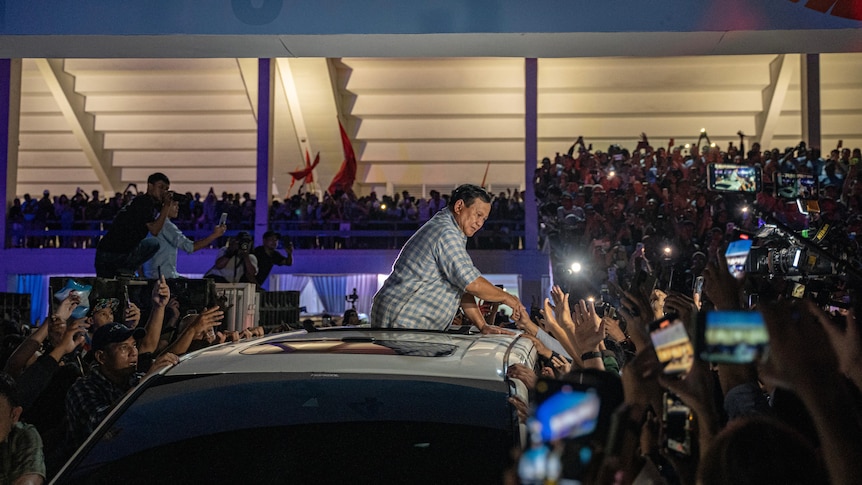 A middle-aged Indonesian man and presidential candidate surrounded by voters with phones