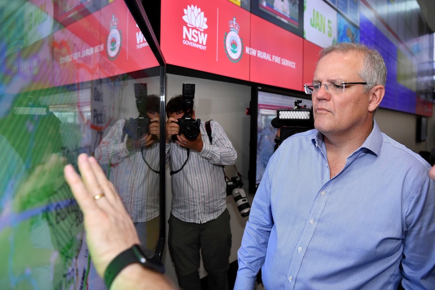 Scott Morrison looks at a screen at the RFS headquarters as a photographer and cameraman stand behind him