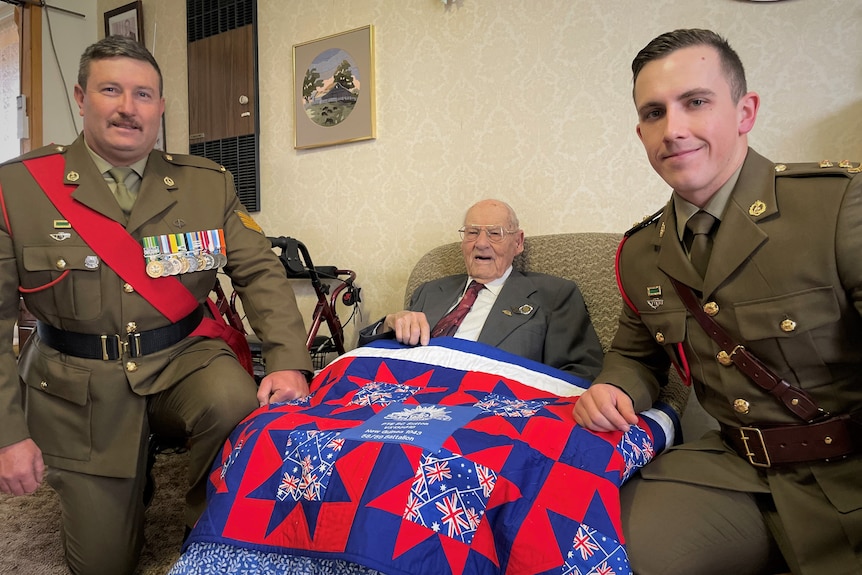 Two younger men in army uniforms and an old man with a blanket