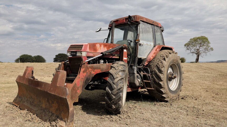 A tractor sits on dry land under grey clouds.