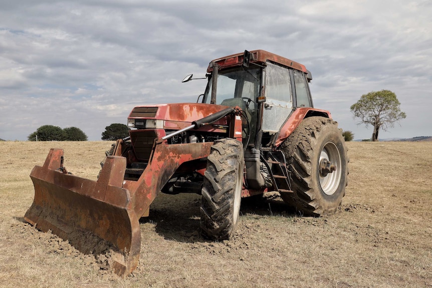 A tractor sits on dry land under grey clouds.