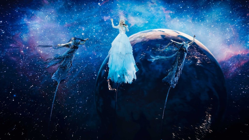 Three performers suspended on tall poles with an image of the Earth behind them at Eurovision.