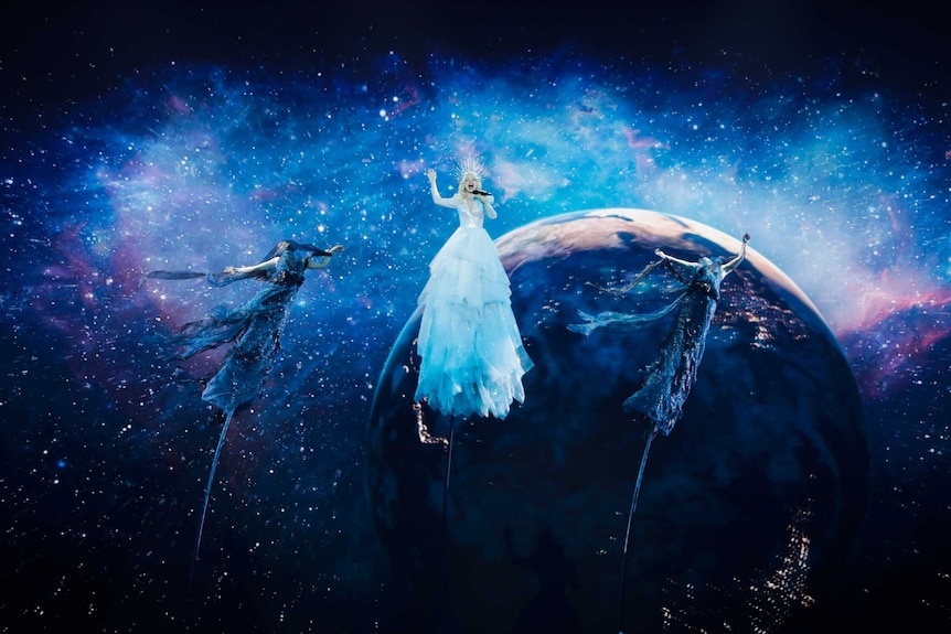 Three performers suspended on tall poles with an image of the Earth behind them at Eurovision.