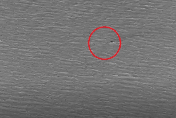 A black and white aerial photograph of an ocean rescue with a red circle highlighting a vessel. 