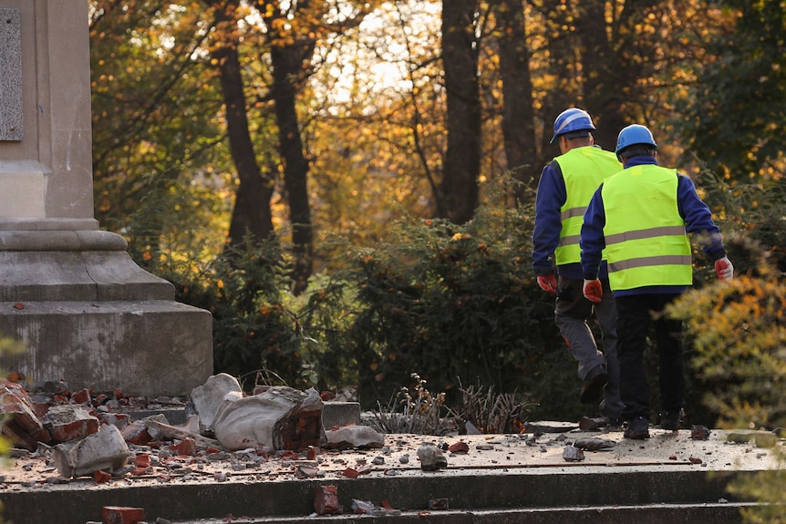 Workers in high-visibilty vets walk across concrete with a damaged monumnet laying on it.