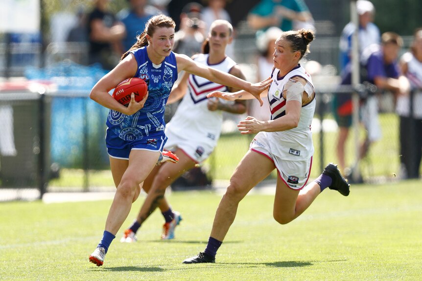Aileen Gilroy runs with the ball while fending off a defender during an AFLW match.
